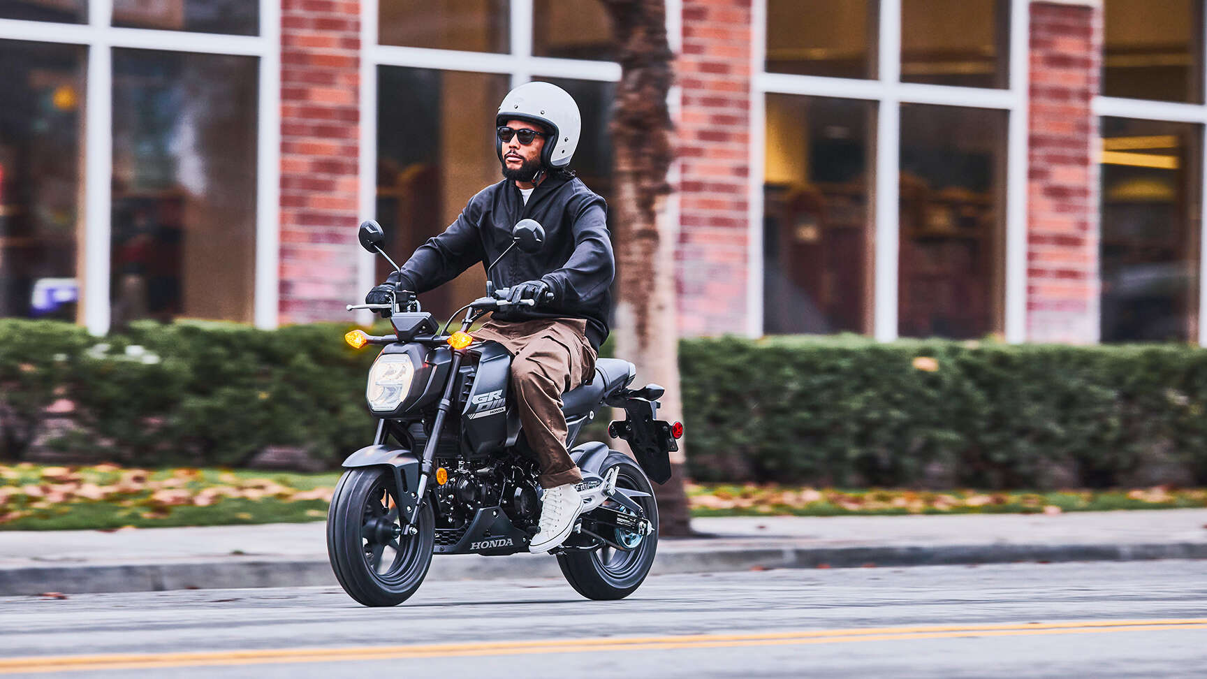 MSX125 Grom fekete színű, parkoló helyzetben, mellette motorosok